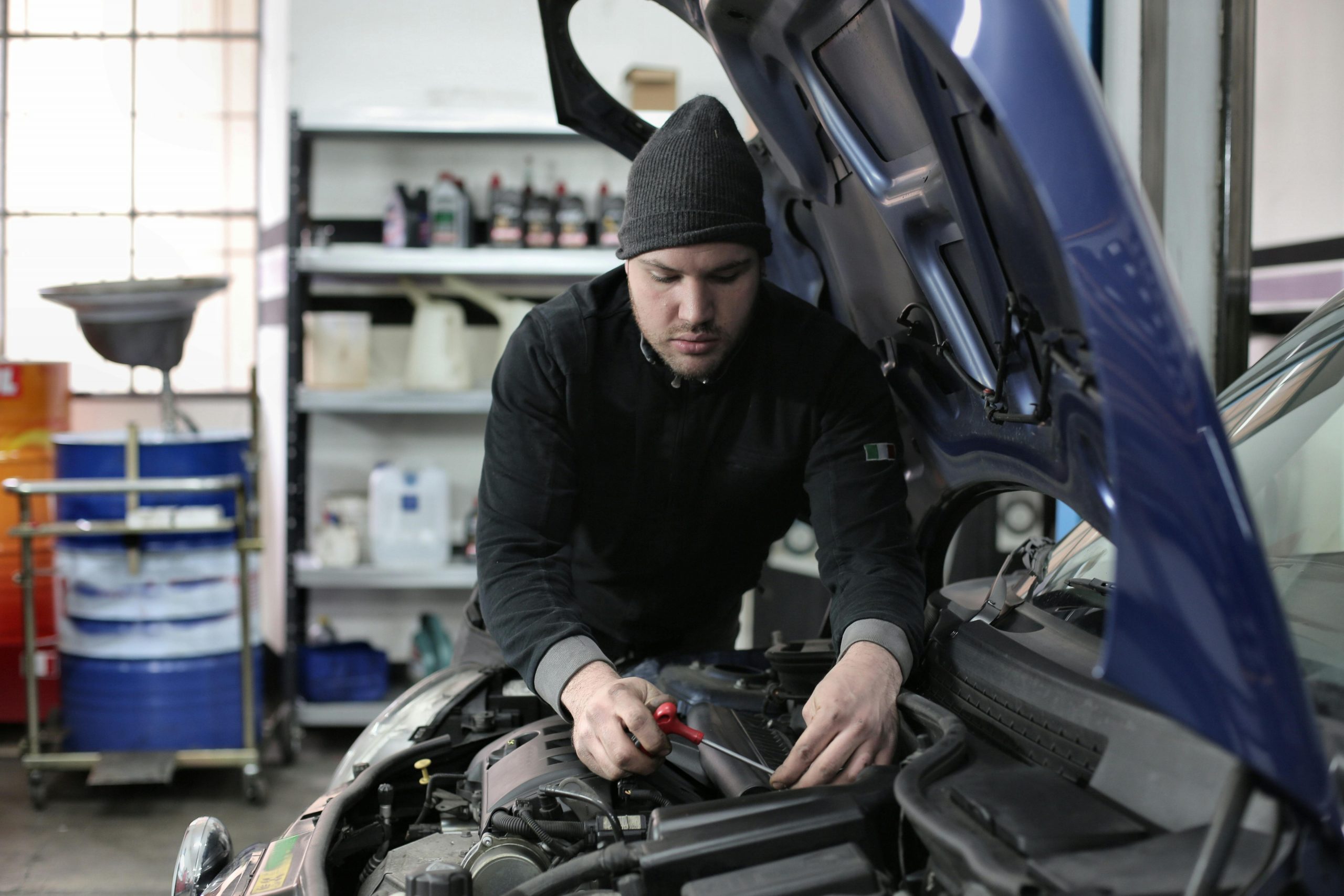 mechanic working under the hood of a blue car, fixing the engine